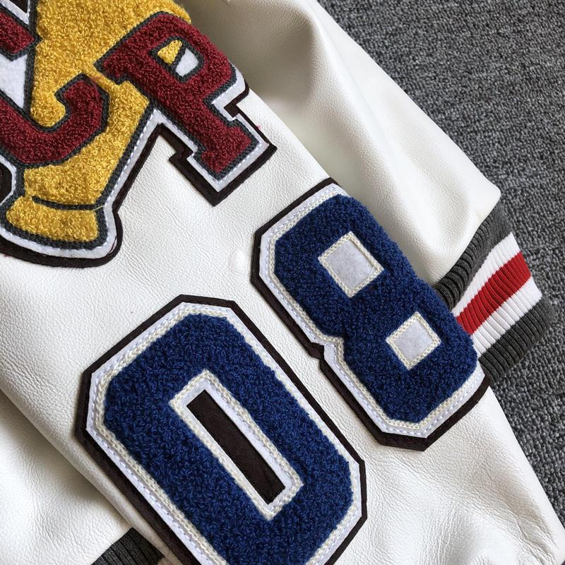 Close-up of textured number and letter patches on a white varsity jacket sleeve with a striped ribbed cuff
